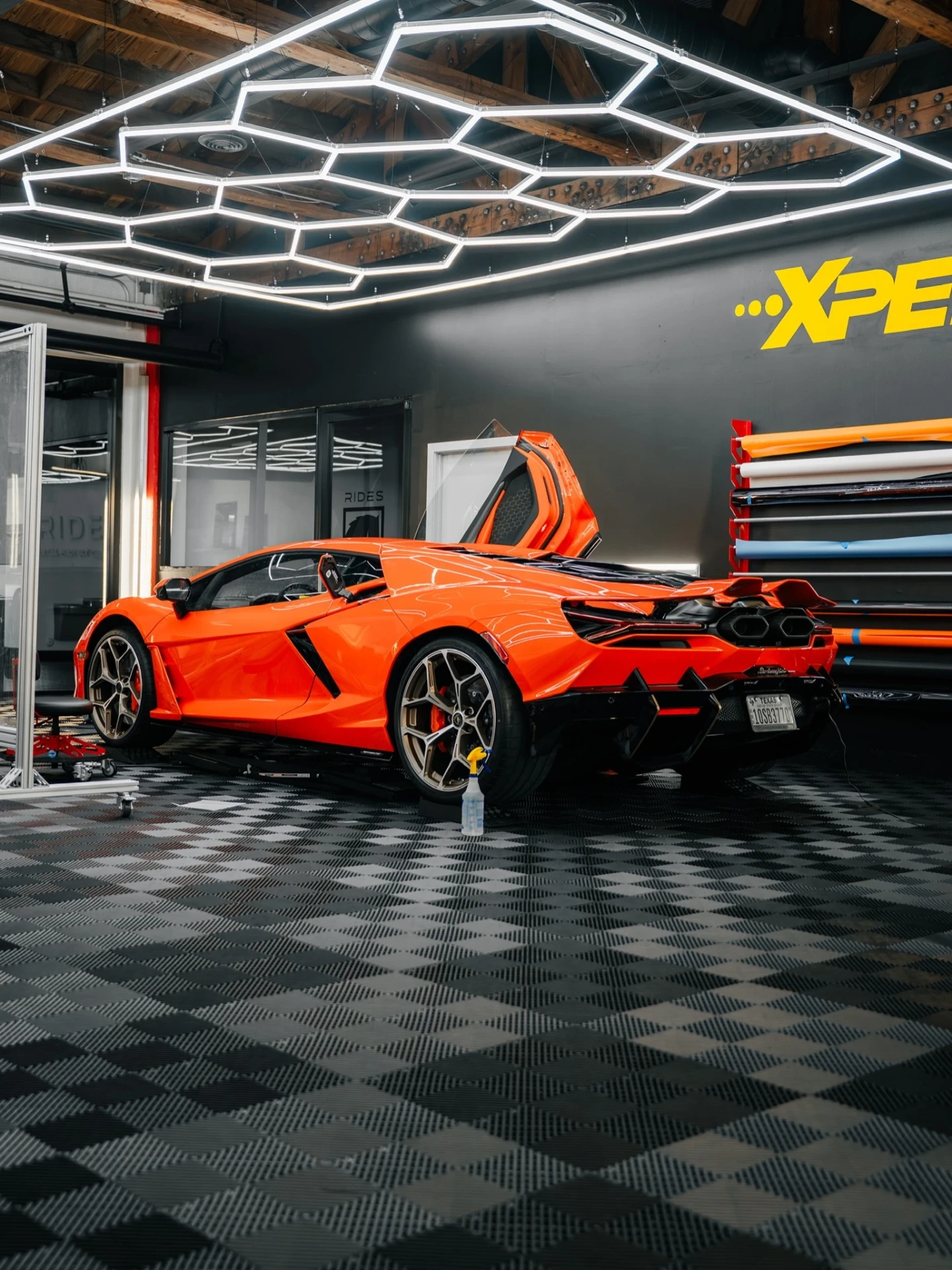 Orange Lamborghini in the Rides Miami bay beside racks of XPEL film