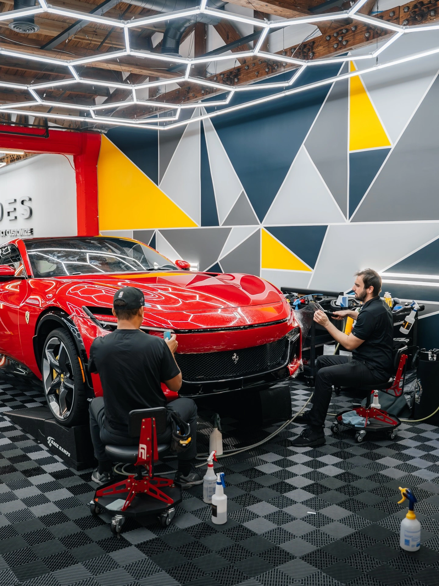 Two Rides Miami installers fitting paint protection film to a red Ferrari under hexagon lighting